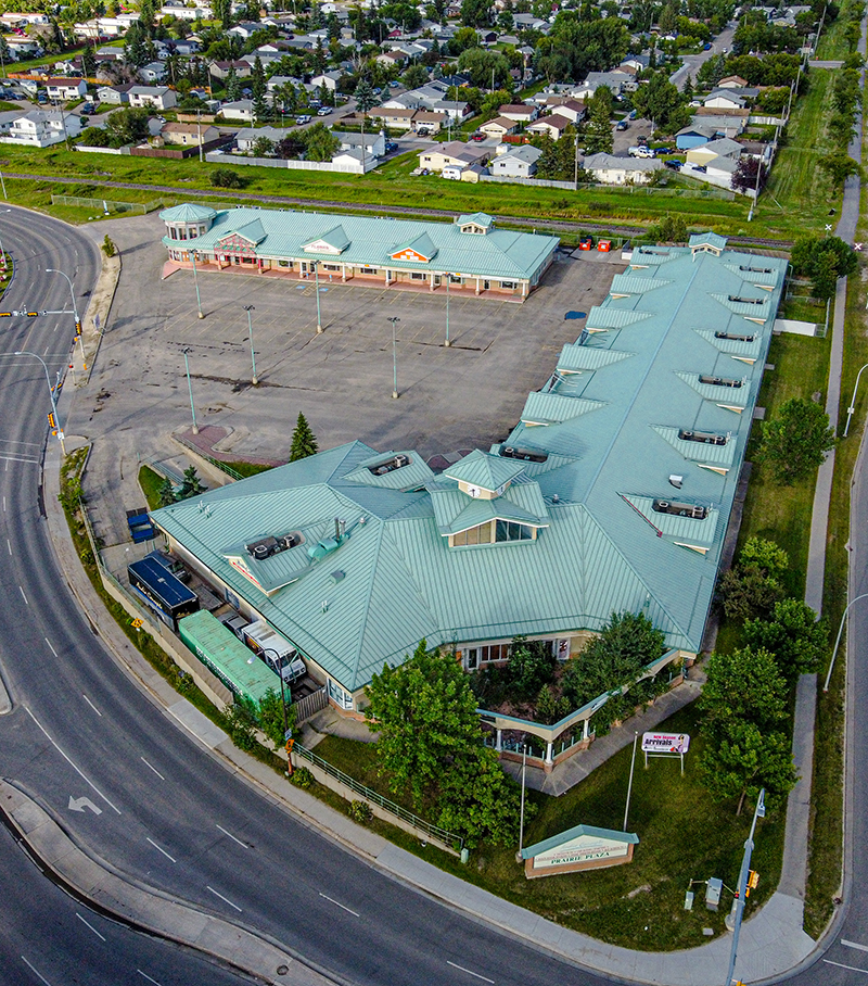 Aerial photo of Grande Prairie commercial property complex, Prairie Plaza. Building has green roof with red brick walls, large parking lot.